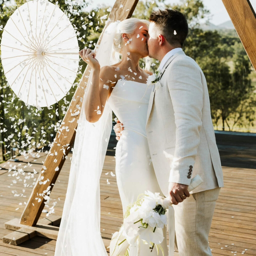 Newlyweds sharing a kiss beneath a white parasol